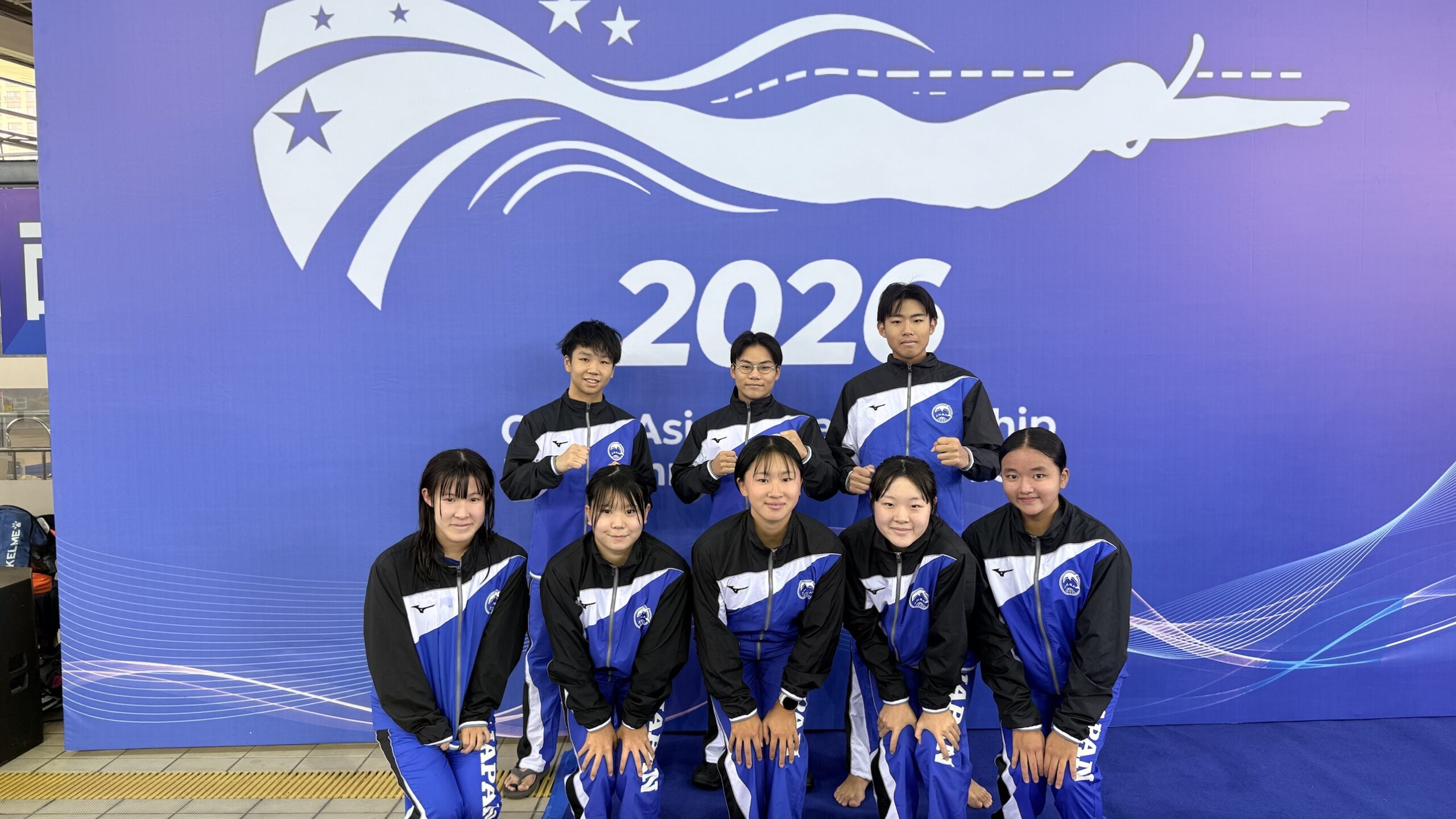 2026アジアジュニア選手権に出場するジュニア日本代表8名。海安の会場で大会ロゴの前に並ぶ集合写真